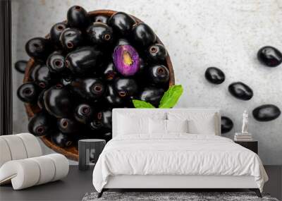 Black ripe Syzygium cumini fruits. Dark black java plum in a wood bowl at isolated white background. Green mint leaf on top of some large java plums. Wall mural