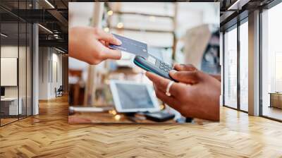 Closeup of unknown mixed race customer using a wireless credit card machine to pay for her coffee. African american barista assisting a woman in a cafe. Contactless paying system during covid pandemic Wall mural