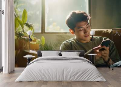 Happy handsome man Asian checking social media holding smartphone sitting on a sofa at home. Smiling young man using mobile phone app playing game, shopping online, generative ai Wall mural