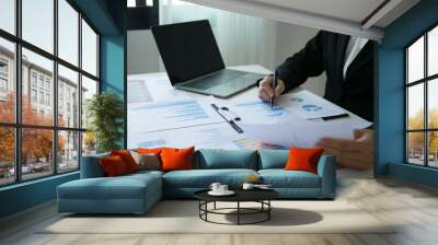 Asian businesswoman holding a pen sits at a table and reads a financial graph showing results about the investment and planning process of successful business growth Wall mural