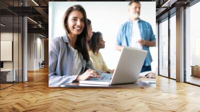 Beautiful business lady is looking at camera and smiling while working in office Wall mural