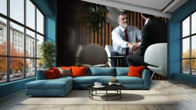 Business partnership meeting in office. Mature businessman shake hands with a younger colleague. Wall mural