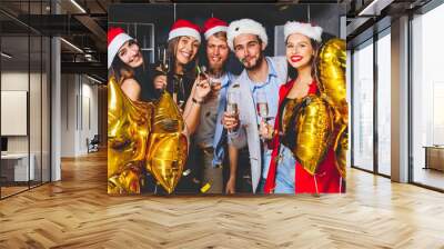 Celebrating New Year together. Group of beautiful young people in Santa hats throwing colorful confetti and looking happy. Wall mural