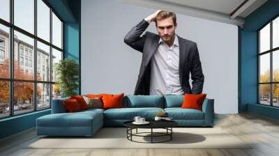 Close up portrait of a handsome young businessman dressed in suit isolated over gray background, looking away. Wall mural