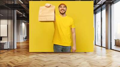 Delivery man holding paper bag with food on yellow background. Wall mural