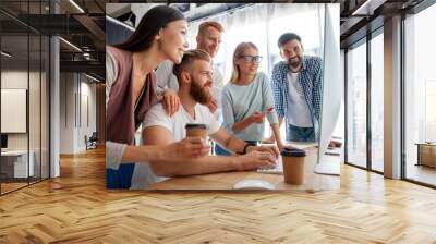 Discussing successful project. Group of young cheerful business people working and communicating while sitting at the office desk together with colleagues sitting in the background. Wall mural