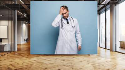 Doctor young man, medical professional terrified and nervous expressing anxiety and panic gesture, isolated over blue background. Wall mural