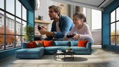 family, gaming and entertainment concept - happy father and little daughter with gamepads playing video game at home. Wall mural