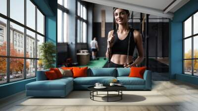 Fit and healthy woman standing at gym with skipping rope. Sportswoman resting after workout. Wall mural