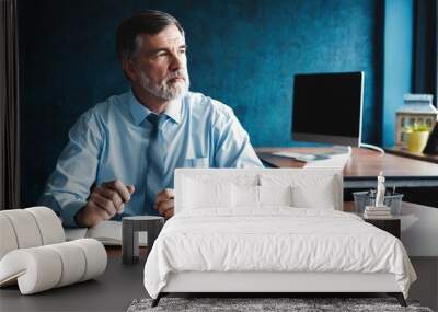 Focused mature businessman deep in thought while sitting at a table in modern office. Wall mural