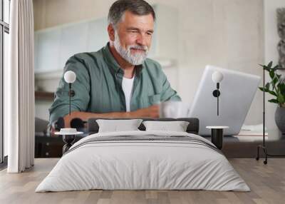 Handsome mature man in casual suit sitting at the table in home office and working at laptop Wall mural