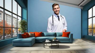 Happy young doctor offering you orange isolated over light blue. Wall mural