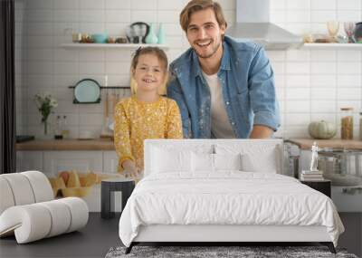 Joyful dad and daughter having fun while kneading dough on kitchen table, baking together Wall mural