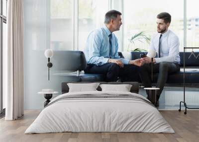 Mature businessman using a digital tablet to discuss information with a younger colleague in a modern business lounge. Wall mural