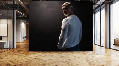 Middle-aged good looking man in white t-shirt posing in front of a black background with copy space. Wall mural