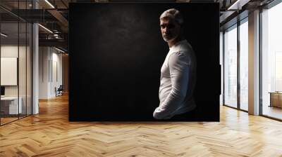 Middle-aged good looking man in white t-shirt posing in front of a black background with copy space. Wall mural