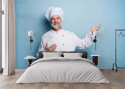 Portrait of a happy chef cook showing copyspace on the palms isolated on light blue background. Wall mural