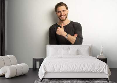 Portrait of cheerful man in casual clothing smiling and showing thumbs up at camera isolated over white Wall mural