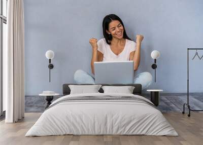 Portrait of excited young casual girl celebrating success while sitting with laptop computer isolated over gray background. Wall mural