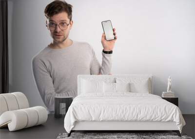 Portrait of happy young man pointing with his finger on the screen of his smartphone on white background. Wall mural