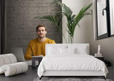 Portrait of young man sitting at his desk in the office Wall mural