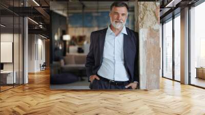 Positive confident mature executive man smiling and looking at camera while standing in office Wall mural