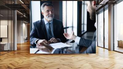 Senior and junior businessman discuss something during their meeting, office background. Wall mural