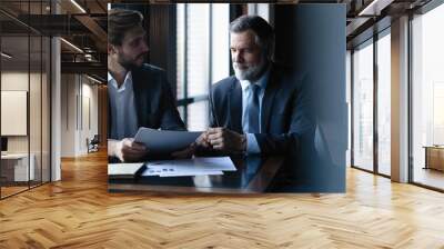 Senior and junior businessman discuss something during their meeting, office background. Wall mural