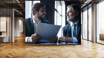 Senior and junior businessman discuss something during their meeting, office background. Wall mural