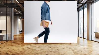 side view of a smiling young casual man walking, student with book ang notes on white background. Wall mural