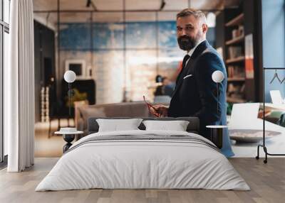 Stylish businessman standing near table in the office and reading documents Wall mural