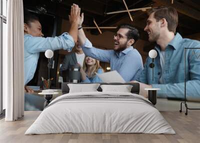 Two cheerful young business people giving high-five while their colleagues looking at them and smiling Wall mural