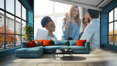 Two cheerful young business people giving high-five while their colleagues looking at them and smiling Wall mural