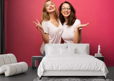 Two exited woman having fun and raising hands up. Standing on pink background. Lucky mood. Wall mural