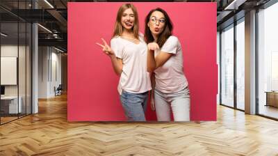 Two exited woman having fun and raising hands up. Standing on pink background. Lucky mood. Wall mural