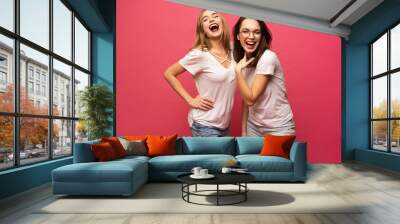 Two exited woman having fun and raising hands up. Standing on pink background. Lucky mood. Wall mural