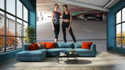 Two happy smiling young athletic woman walking outdoors together after sport training, talking and hugging each other Wall mural