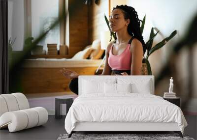 Young black woman doing yoga at home in the lotus position. Wall mural