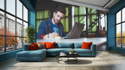 Young businessman working in office, sitting at desk, looking at laptop computer screen, smiling Wall mural