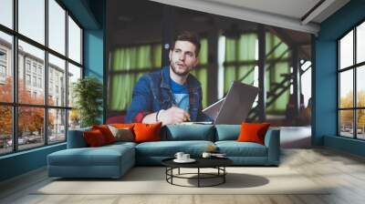 Young businessman working in office, sitting at desk, looking at laptop computer screen, smiling Wall mural