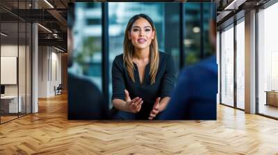 A confident businesswoman presents her ideas while discussing with two colleagues in a contemporary office. Wall mural