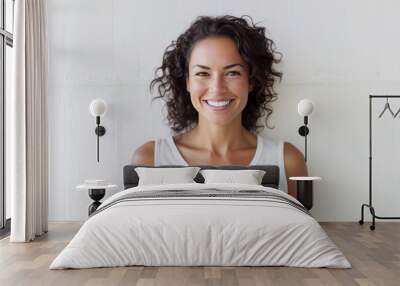 Smiling 40 year old brunette woman in white t-shirt standing in front of a white wall. Wall mural