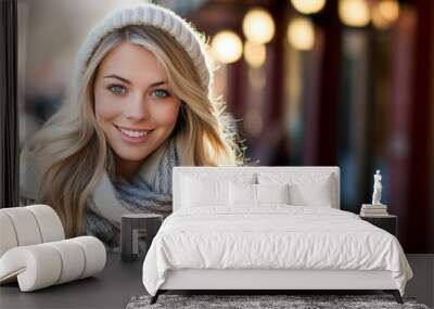 Smiling blonde woman wearing coat hat and scarf posing on the street in winter. Wall mural