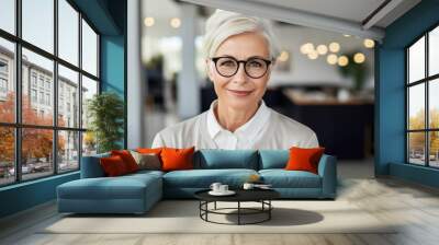 Smiling senior woman with white hair and white clothing posing in an office. Wall mural