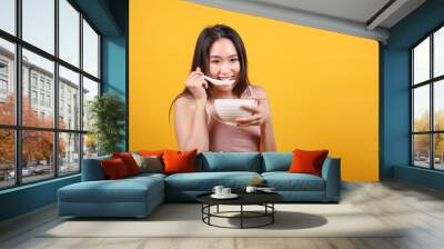 Beautiful young south east Asian woman holding chines empty chopstick Chinese soup spoon bowl utensil pretend acting posing see eat taste smell feed offer satisfaction yummy yellow orange background Wall mural