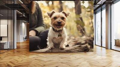 A cheerful small dog sitting on a log in a forest, surrounded by autumn foliage, exuding joy and companionship. Wall mural