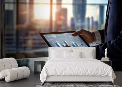 Businessman hand using a touchscreen tablet with financial charts displayed, with a modern office environment in the background Wall mural