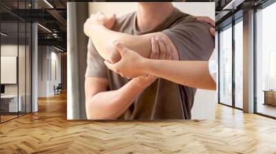 Female physiotherapists provide assistance to male patients with elbow injuries examine patients in rehabilitation centers. Physiotherapy concepts Wall mural