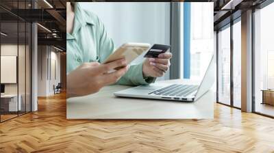 The businesswoman's hand is holding a credit card and using a smartphone for online shopping and internet payment in the office Wall mural