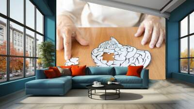 Elderly woman hands putting missing white jigsaw puzzle piece down into the place as a human brain shape. Creative idea for memory loss, dementia, Alzheimer's disease and mental health concept. Wall mural